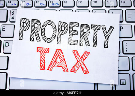 Handwritten text caption showing Property Tax. Business concept writing for Estate Income Taxation written on sticky note paper on white keyboard back Stock Photo
