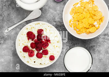 Cottage cheese in bowl with frozen raspberry and cup of cornflakes, milk in glass on a light background. Top view. Food background Stock Photo