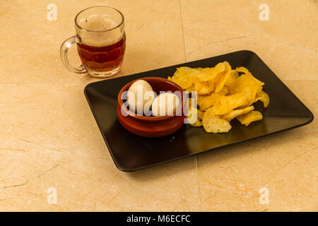Two pickled eggs in ceramic bowl, served with crisps or chips and half pint of English beer. Stock Photo