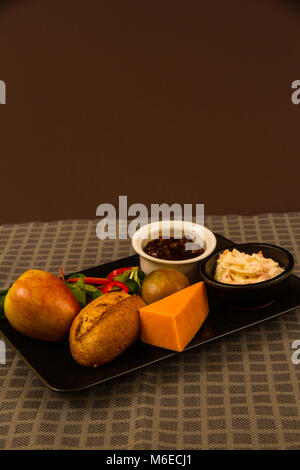 Ploughman’s lunch with red leicester cheese, pickle, pickled onion, salad, coleslaw and bread roll and apple. Stock Photo