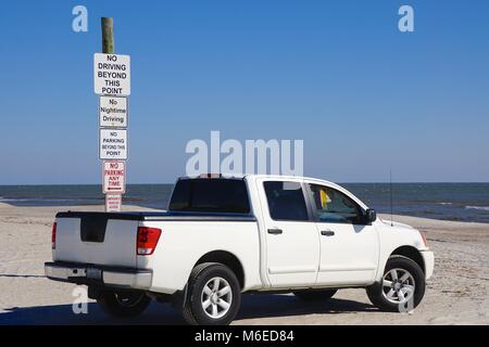 Amelia Island, Florida, USA: Pick-up truck parked on a beach next to a pole with a stack of signs warning of local regulations. Stock Photo