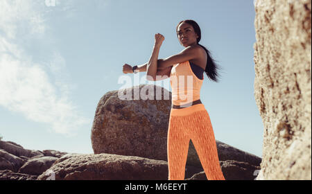 fitness woman doing hands stretching workout at the rocky beach. African female doing arms workout at the beach. Stock Photo