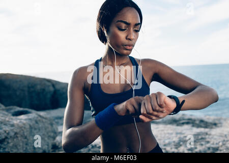 Fit female runner using smart watch to monitor her performance. African Woman setting fitness app on her smartwatch before running session. Stock Photo