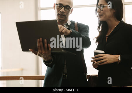 Businessman pointing at laptop and discussing something with coworker while standing at office. Business team working together in office, discussing s Stock Photo