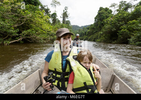 Mother and son tourists wearing life jackets in traditional wooden boat on the river in the oldest rainforest in the world, Taman Negara, Malaysia Stock Photo