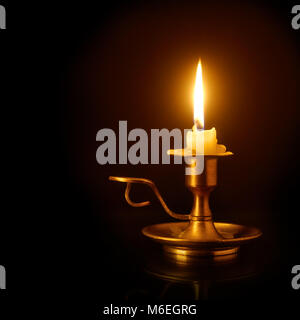 Burning candle on the old brass candlestick over black background Stock Photo