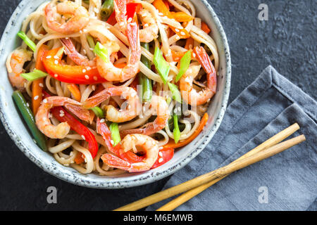 Shrimps, vegetables, noodles and black wok on grey textured table ...