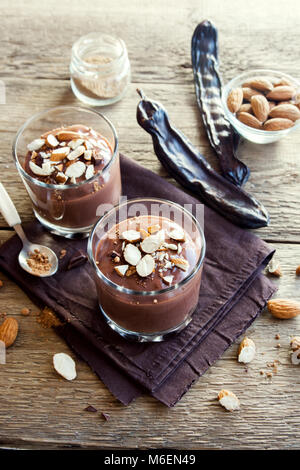 Chocolate (Carob) Mousse topped with Almond in glasses over wooden background close up - delicious homemade Raw Vegan Chocolate Pudding with Nuts and  Stock Photo