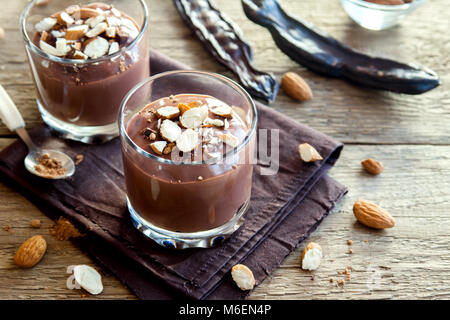 Chocolate (Carob) Mousse topped with Almond in glasses over wooden background close up - delicious homemade Raw Vegan Chocolate Pudding with Nuts and  Stock Photo