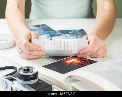 Young engaged or married female person sitting at white desk  holds photograph and chooses pictures for family photo album Stock Photo