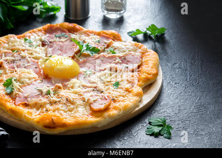 Pizza Carbonara on black stone background. Italian Pizza Carbonara with Bacon, Egg and Cheese, copy space. Stock Photo