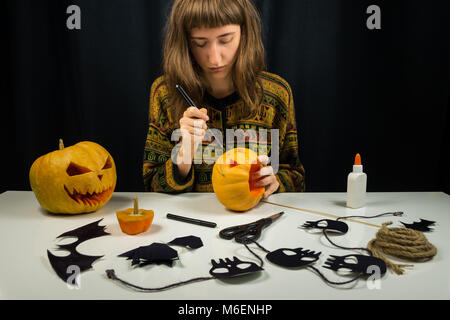 Girl makes halloween decorations including paper figures, skulls and cuts scary faces of pumpkins Stock Photo