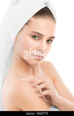 Woman with clean face and towel on her head applying moisturizer cream at shoulders. Isolated. Stock Photo