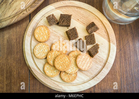 Top view of dry biscuits and corn bread as food sample. Biscuits and dark bread for degustation on a wood plate and water jar, flat lay Stock Photo