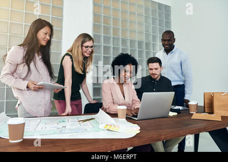 Diverse group of business colleagues smiling and having a discussion while working together at a desk in a modern office Stock Photo