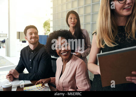 Group of diverse business colleagues smiling while working together around a desk in a modern office Stock Photo