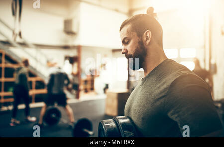 Fit and focused young man in sportswear standing in a gym selecting weights before a workout Stock Photo