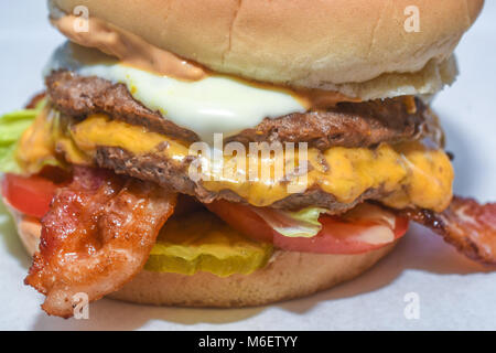Close up of bacon cheeseburger with melted cheese, lettuce and tomato representing classic American fast food meal. Stock Photo