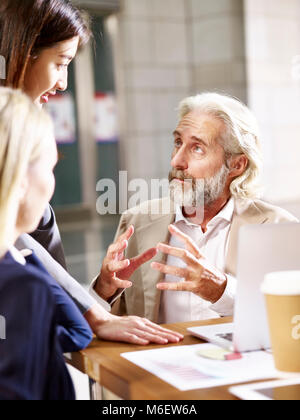 caucasian european senior executive talking to two business women in office. Stock Photo