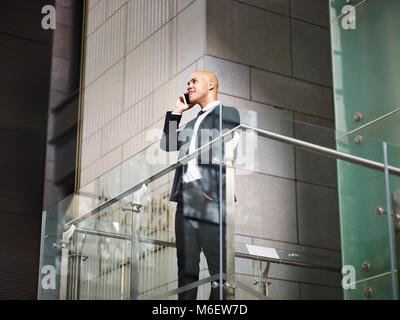 latin american corporate executive business man standing on top of stairs making a call using mobile phone in modern office building, low angle view. Stock Photo