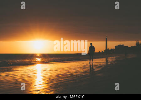 Walker on seashore with lighthouse during sunset in Maspalomas, Gran Canaria Island. Stock Photo