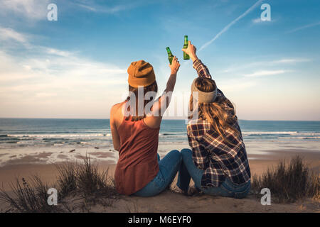 Two best friends sitting on the coastline toasting to friendship