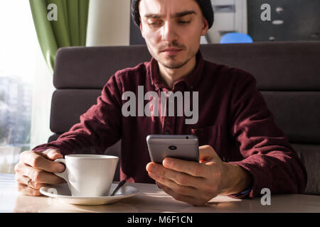 Worried young man with smartphone having coffee at cafe Stock Photo