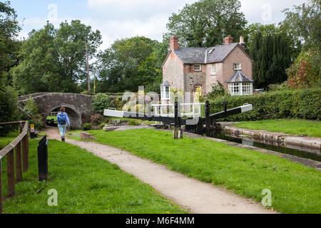 Woman walking along the towpath past locks on the Montgomery canal while walking Offa's Dyke long distance footpath in Shropshire near  Llanymynech Stock Photo