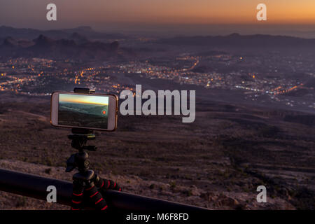 Cellphone mounted on the rail taking timelap videos of the illuminated Al Hamra village at sunset Stock Photo