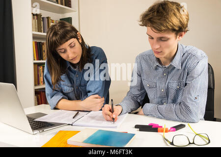 Male and female students or co-workers sitting at table. Two people (young man and woman) do assignment or project together at home office desk. Stock Photo