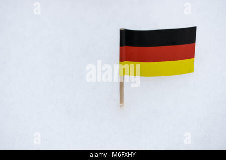 Small Germany flag made from paper with brown toothpick on white snow background. Stock Photo