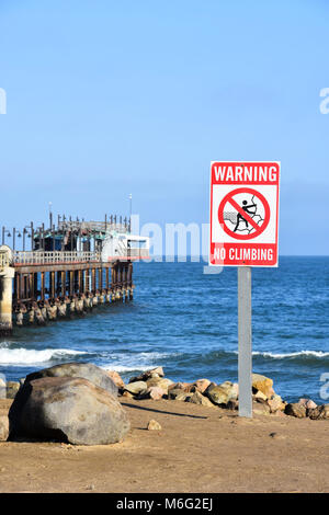 The jetty and a sign warning against climbing near the beach of Swakopmund Namibia Southern Africa in the early morning sun at the Atlantic Ocean agai Stock Photo