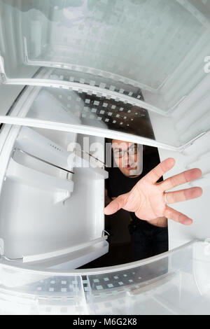 Funny scene of hungry young man opening the door of the fridge and reaching for food, view from inside the freezer Stock Photo