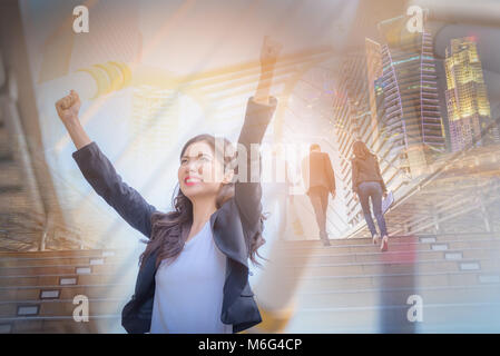 Double exposure image of business woman smiling with arms up celebrate on blurred city background. Business success concept. Stock Photo