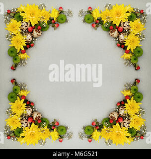Easter decorative frame of yellow, green and white flowers with quail eggs on gray paper background. Flat lay, top view. Stock Photo
