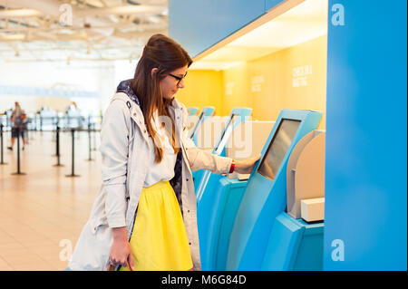 Young woman at self service transfer area doing self-check-in at automated machine with touchscreen display in airport terminal building Stock Photo