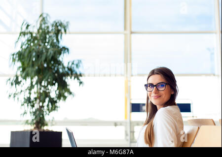 Casual woman working on laptop in airport hall. Woman waiting his flight at airport terminal, sitting on chair and typing on the laptop. Stock Photo