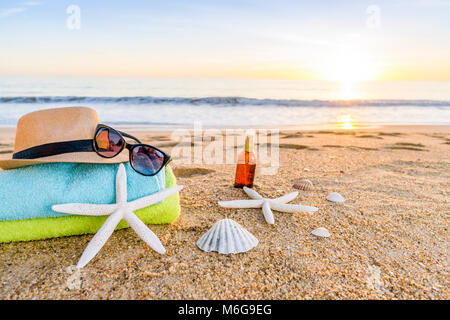 Summer accesories as sunglasses, towels, hat, sun block, shells and starfish on sandy beach in Portugal Stock Photo