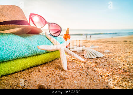 Summer accesories as sunglasses, towels, hat, sun block, shells and starfish on sandy beach in Portugal Stock Photo