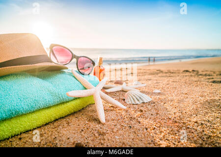 Summer accesories as sunglasses, towels, hat, sun block, shells and starfish on sandy beach in Portugal Stock Photo
