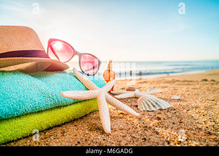 Summer accesories as sunglasses, towels, hat, sun block, shells and starfish on sandy beach in Portugal Stock Photo