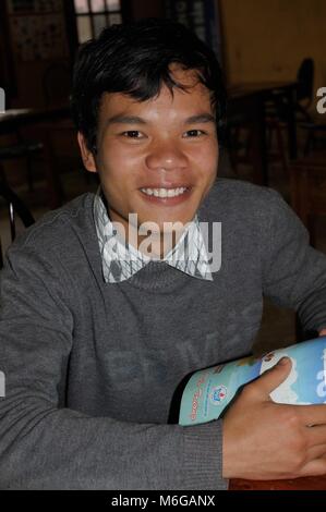 Young Vietnamese boy wearing a grey sweater, holding a book and smiling and happy in english language classroom. Stock Photo