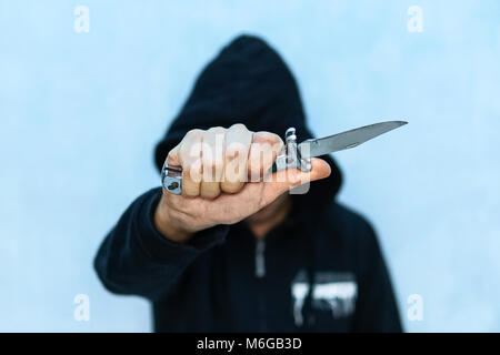 A young man in a hoodie holding a knife symbolizing youth crime. Crime concept. The threat of a cold weapon. A terrorist from ISIS with a knife. A pri Stock Photo