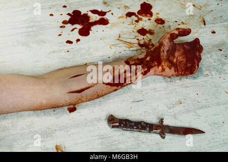 A bloody hand with a knife on a white vintage wooden dirty floor. The concept of household crimes and domestic violence. Crime scene murder victim han Stock Photo
