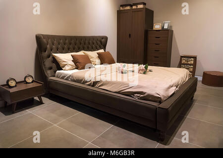 Large master bedroom with a large bed with a cushioned headboard. flowers on the bed. The Bridal Suite in an expensive hotel. Bedside table, cupboard, Stock Photo