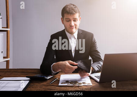 Sad Businessman Checking His Wallet With Coins And Laptop On Wooden Desk Stock Photo