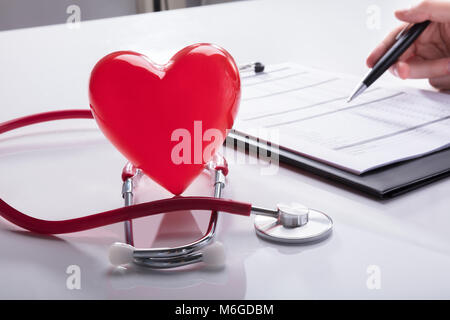Stethoscope And Red Heart Near Doctor's Hand Analyzing Report On Clipboard Stock Photo