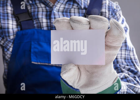 Close-up Of Workman Hands With Gloves Showing Blank Card Against Grey Background Stock Photo