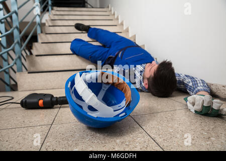 Unconscious Handyman Lying On Staircase With Helmet And Drill On Floor Stock Photo
