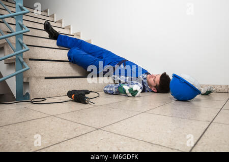 Unconscious Handyman Lying On Staircase With Helmet And Drill On Floor Stock Photo